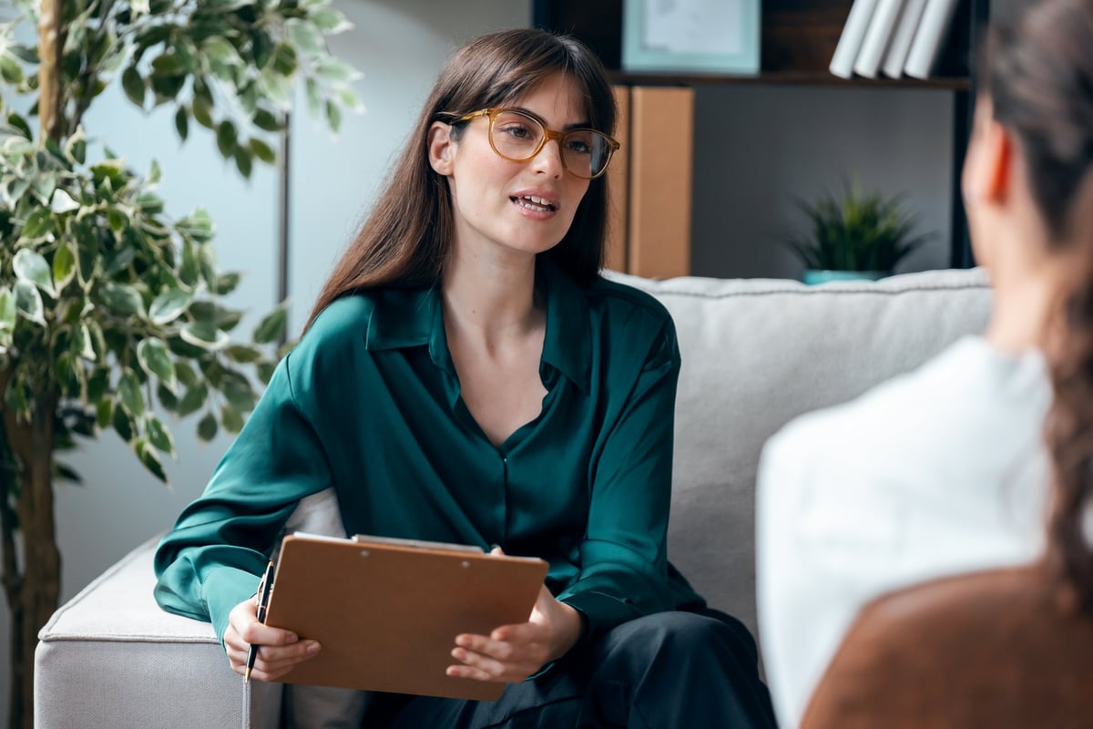 Shot of female psychologist giving therapy to a patient while taking notes, sitting on the couch in the psychology office